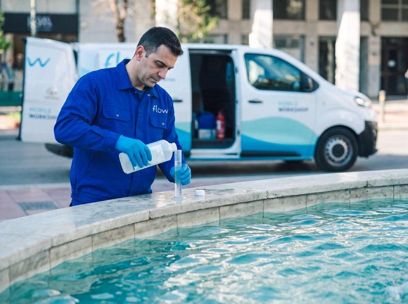 Τεχνικός της Flow με μπλε στολή ελέγχει και δοσομετρεί απολυμαντικό για το νερό σιντριβανιού